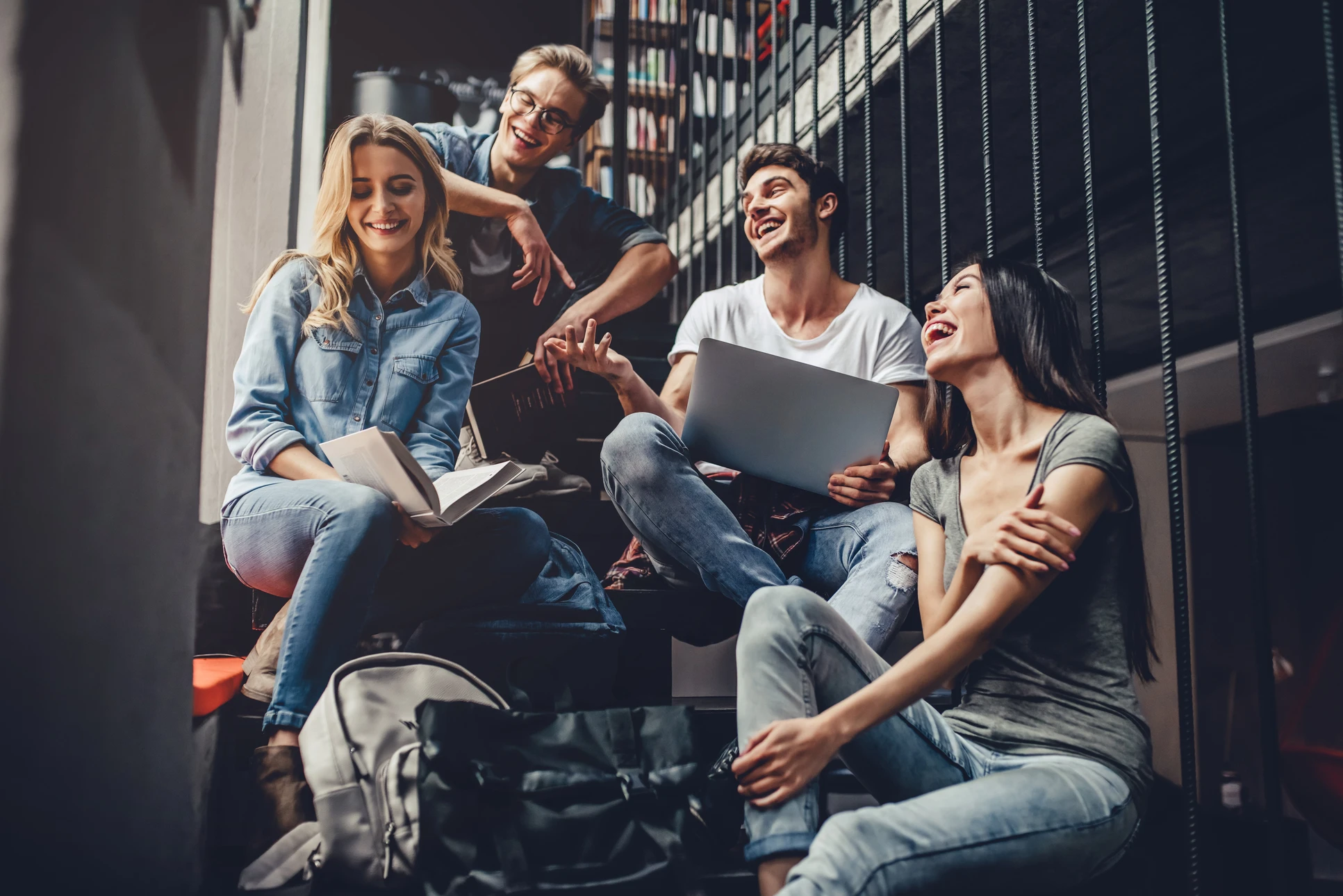 Quatre jeunes adultes souriants assis sur des marches dans un environnement urbain moderne avec immeubles en arrière-plan